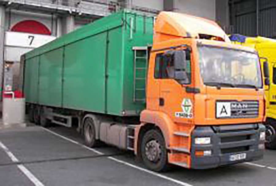 Oranger Lkw mit grünem Container an Verladerampe der Umladestation